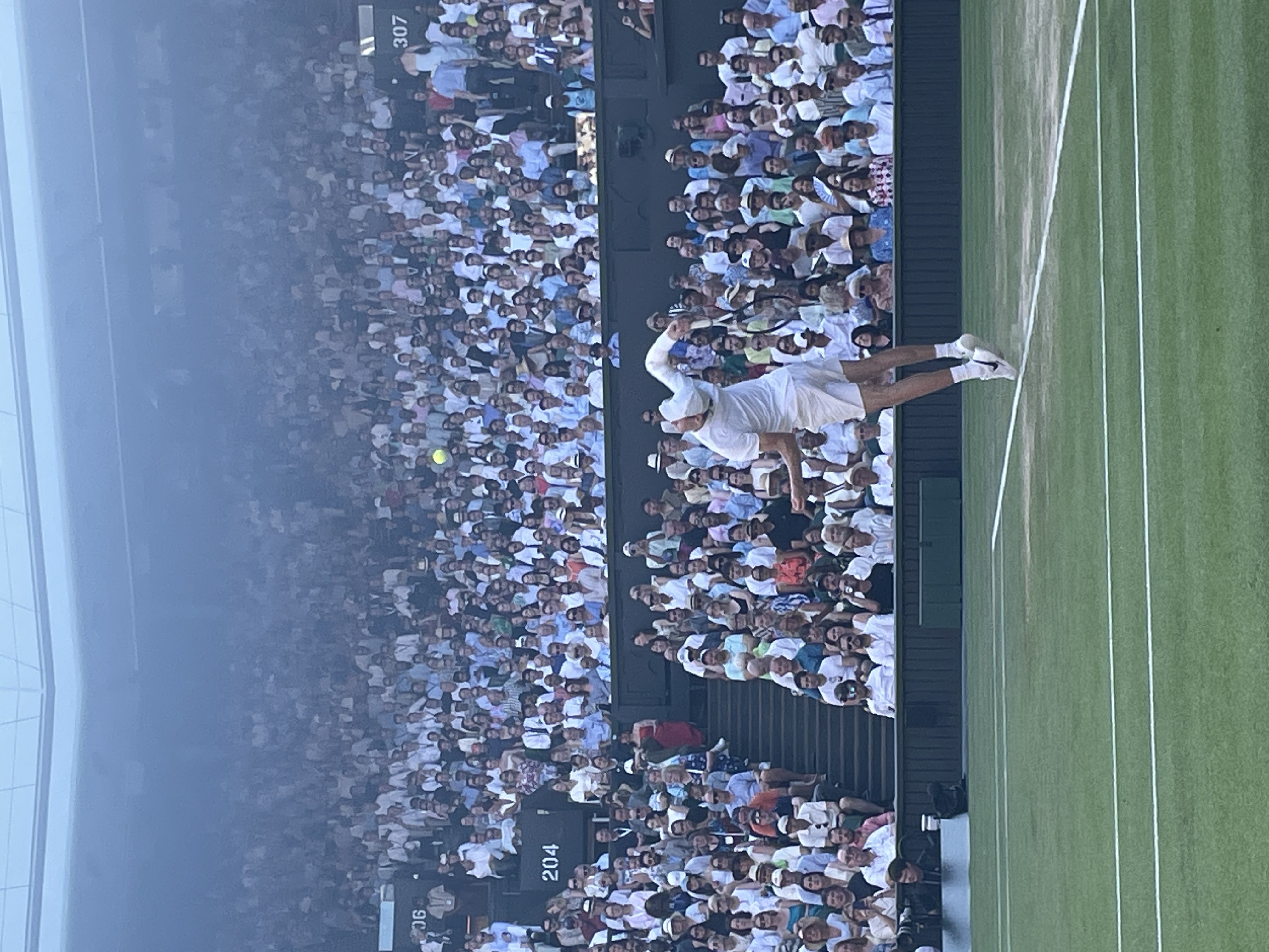 A tennis player serving on a grass court at Wimbledon in front of spectators.